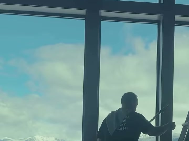 An Allen’s crew member cleaning floor-to-ceiling windows at the Tumble Creek private club, with snow-capped mountains beyond.