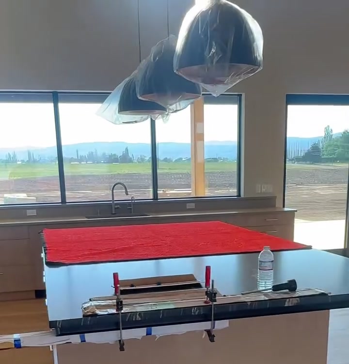 A newly built kitchen with pendant lights still bagged in plastic and the island under a protective cover, before the post-construction clean.